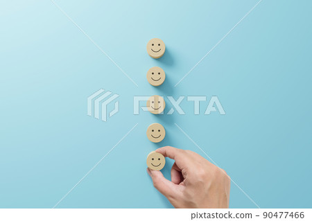 Hand choose wooden cube block with icon face smile on light blue background 90477466