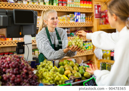 Female grocery store worker handing grape to customer after payment at checkout closeup Female grocery store worker handing grape to customer after payment at checkout closeup 90478365
