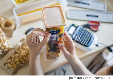 Closeup female hands sticking label on plastic package pasta. Storage organization of food products 90480094