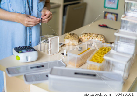 Focused female professional space organizer marking plastic case boxes for pasta storage at kitchen 90480101