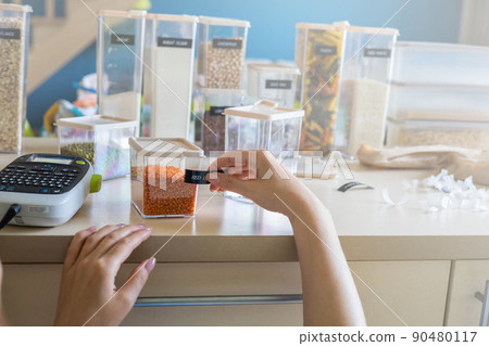 Closeup female hands applying printing sticker with name red lentils on transparent plastic case box 90480117