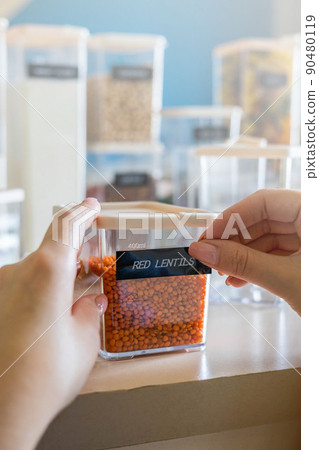 Closeup female hands applying printing sticker with name red lentils on transparent plastic case box 90480119