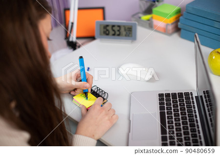 A young girl is scrawling words in English on small pieces of paper. 90480659