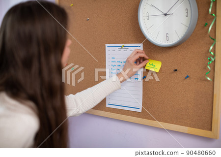 A teenager tapes a piece of paper to the board with a word written in English. A teenager tapes a piece of paper to the board with a word written in English. 90480660