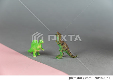 Dinosaur miniatures standing on a gray-pink background. Small green figures of predatory dinosaurs standing on their hind legs. Selective focus. Dinosaur miniatures standing on a gray-pink background. Small green figures of predatory dinosaurs standing on their hind legs. Selective focus. 90480965