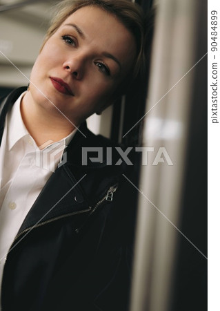 young caucasian short haired blond woman wearing leather jacket, jeans and glasses leaned on door in car of metro, looking aside. Image with selective focus young caucasian short haired blond woman wearing leather jacket, jeans and glasses leaned on door in car of metro, looking aside. Image with selective focus 90484899