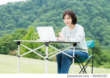 A woman looking at a computer while drinking coffee outdoors A woman looking at a computer while drinking coffee outdoors 90485387