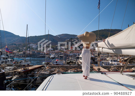 Beautiful young blond woman standing on catamaran at sunny summer day at Hydra marina bay, Greece Beautiful young blond woman standing on catamaran at sunny summer day at Hydra marina bay, Greece 90488927