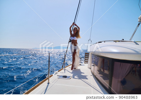 Beautiful young blond woman in bikini standing on catamaran at sunny summer day Beautiful young blond woman in bikini standing on catamaran at sunny summer day 90488963