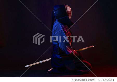 Close up shot, Kendo fighter wearing in an armor, traditional kimono, helmet practicing martial art with shinai bamboo sword, black background. 90489084