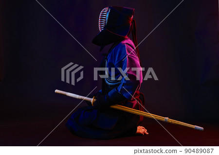 Close up shot, Kendo fighter wearing in an armor, traditional kimono, helmet practicing martial art with shinai bamboo sword, black background. 90489087