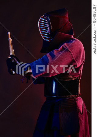 Close up shot, Kendo fighter wearing in an armor, traditional kimono, helmet practicing martial art with shinai bamboo sword, black background. 90489187