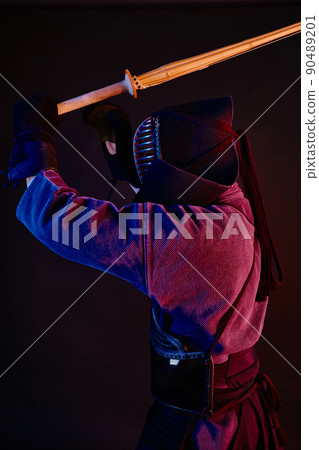 Close up shot, Kendo fighter wearing in an armor, traditional kimono, helmet practicing martial art with shinai bamboo sword, black background. 90489201