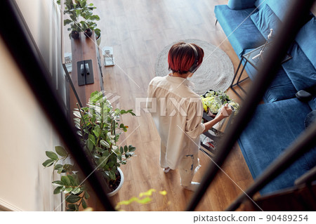 Guy in headphones watering green house plant at home 90489254