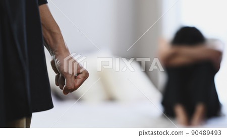 Aggressive man clenching fist in anger with crying woman in background. Concept of domestic family violence 90489493