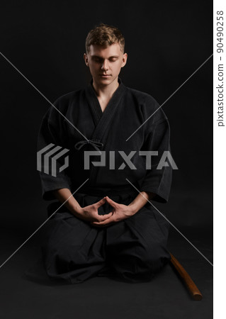 Kendo guru wearing in a traditional japanese kimono is practicing martial art with the shinai bamboo sword against a black studio background. 90490258