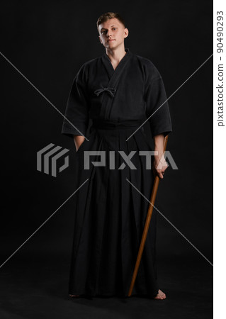Kendo guru wearing in a traditional japanese kimono is practicing martial art with the shinai bamboo sword against a black studio background. 90490293