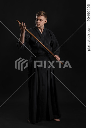 Kendo guru wearing in a traditional japanese kimono is practicing martial art with the shinai bamboo sword against a black studio background. Kendo guru wearing in a traditional japanese kimono is practicing martial art with the shinai bamboo sword against a black studio background. 90490406
