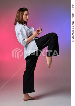 Athletic woman in traditional kimono is practicing karate in studio. 90490495