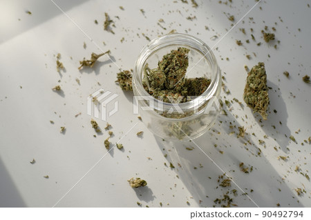 Weed Store. Glass jar with dried cannabis buds on white background with crushed marijuana. 90492794