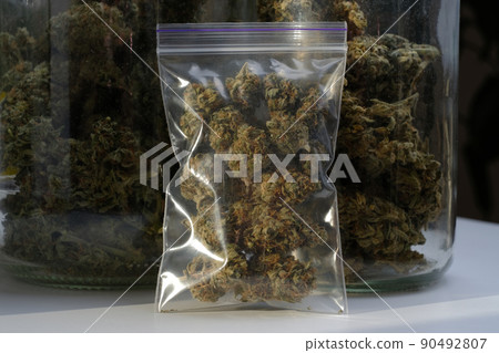 Dry and trimmed cannabis buds stored in a plastic bag on glass jars background with buds. Medical marijuana Dry and trimmed cannabis buds stored in a plastic bag on glass jars background with buds. Medical marijuana 90492807