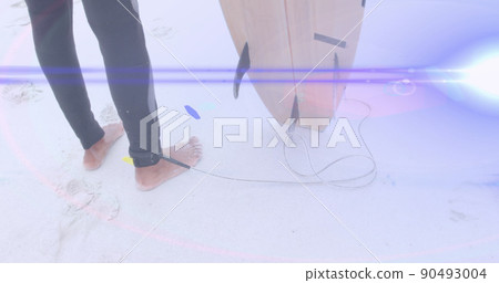 Image of light beams moving over feet of surfer on beach holding surfboard Image of light beams moving over feet of surfer on beach holding surfboard 90493004