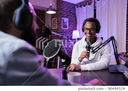 Multiethnic team of people meeting to record podcast episode together, creating online content with live broadcast discussion. Male vlogger talking to adult, livestream production. 90494324