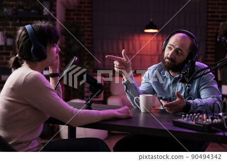 Male presenter interviewing woman on podcast discussion, talking to guest in studio. Young man having conversation with social media blogger, recording show for channel content. 90494342