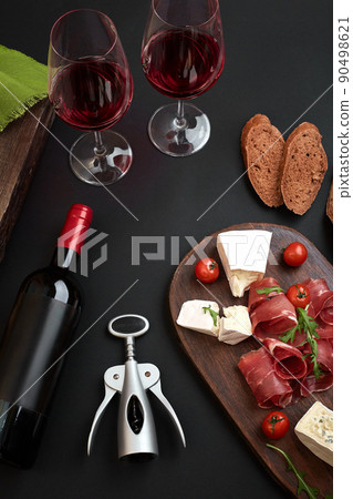 Above overhead view flat lay still life of assortment various cheese and delicatessen with traditional bread and red wine on a old wooden board on black table Above overhead view flat lay still life of assortment various cheese and delicatessen with traditional bread and red wine on a old wooden board on black table 90498621