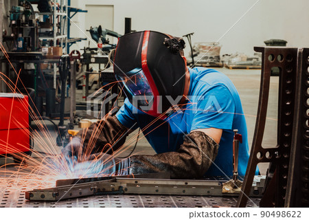 Professional Heavy Industry Welder Working Inside factory, Wears Helmet and Starts Welding. Selective Focus Professional Heavy Industry Welder Working Inside factory, Wears Helmet and Starts Welding. Selective Focus 90498622