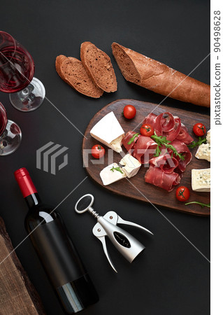 Above overhead view flat lay still life of assortment various cheese and delicatessen with traditional bread and red wine on a old wooden board on black table Above overhead view flat lay still life of assortment various cheese and delicatessen with traditional bread and red wine on a old wooden board on black table 90498628
