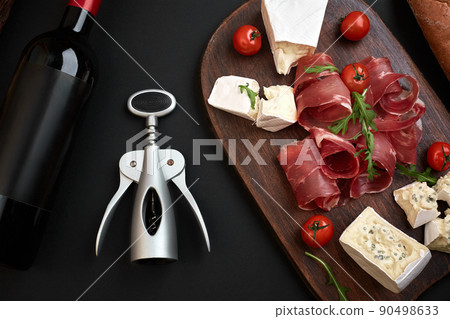 Wine bottle with cheese and traditional sausages on wooden board on black background with copy space Wine bottle with cheese and traditional sausages on wooden board on black background with copy space 90498633