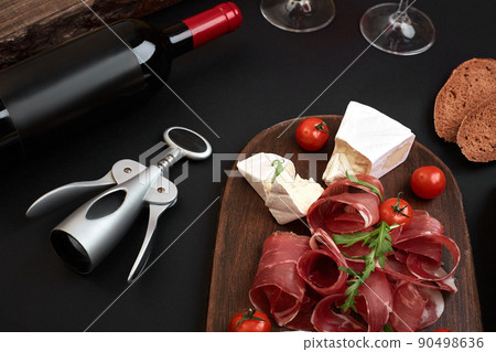 Above overhead view flat lay still life of assortment various cheese and delicatessen with traditional bread and red wine on a old wooden board on black table Above overhead view flat lay still life of assortment various cheese and delicatessen with traditional bread and red wine on a old wooden board on black table 90498636
