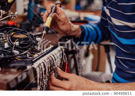 Industrial worker man soldering cables of manufacturing equipment in a factory. Selective focus Industrial worker man soldering cables of manufacturing equipment in a factory. Selective focus 90498651