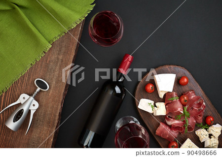 Above overhead view flat lay still life of assortment various cheese and delicatessen and red wine on a old wooden board on black table Above overhead view flat lay still life of assortment various cheese and delicatessen and red wine on a old wooden board on black table 90498666
