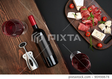 Above overhead view flat lay still life of assortment various cheese and delicatessen and red wine on a old wooden board on black table 90498678