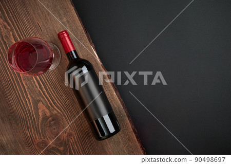 Bottle of wine and one glass on the wooden board on black background. Top view with copy space Bottle of wine and one glass on the wooden board on black background. Top view with copy space 90498697