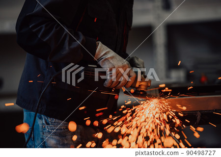 Heavy Industry Engineering Factory Interior with Industrial Worker Using Angle Grinder and Cutting a Metal Tube. Contractor in Safety Uniform and Hard Hat Manufacturing Metal Structures. 90498727