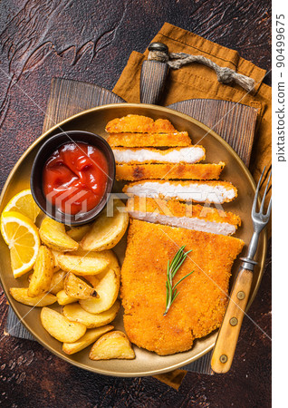 Breaded german weiner schnitzel with potato wedges. Dark background. Top view 90499675