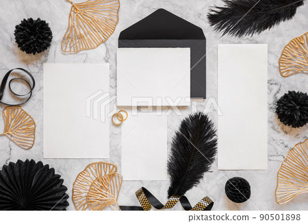 Cards and envelope on marble table near black feathers and golden leaves. Wedding mockup 90501898