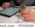 Closeup of a woman holding a silver bitcoin and working with charts on a tablet 90506066