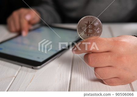 Closeup of a woman holding a silver bitcoin and working with charts on a tablet Closeup of a woman holding a silver bitcoin and working with charts on a tablet 90506066