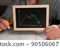 A woman holds a golden bitcoin and a blackboard with a graph. Cryptocurrency. 90506067