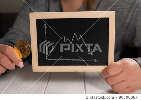 A woman holds a golden bitcoin and a blackboard with a graph. Cryptocurrency. 90506067