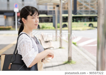 A smiling woman waiting for the bus at the bus stop A smiling woman waiting for the bus at the bus stop 90507322