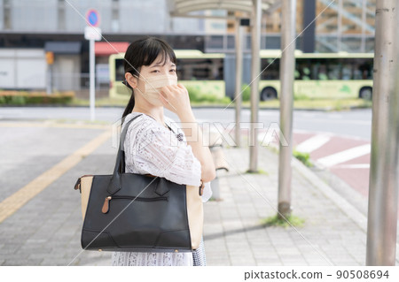 Woman in mask waiting for the bus at the bus stop 90508694