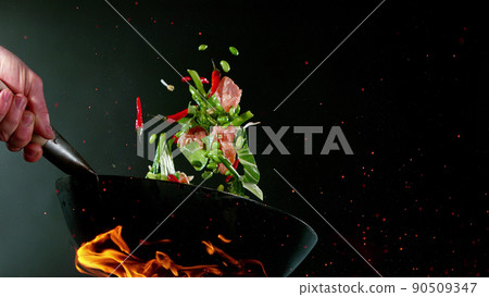 Closeup of chef throwing salmon pieces with vegetable. Closeup of chef throwing salmon pieces with vegetable. 90509347