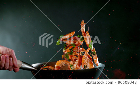 Closeup of chef throwing shrimps from wok pan in fire. 90509348