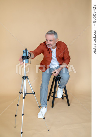 A man in a red jacket sitting on a stool in a studio and making selfie A man in a red jacket sitting on a stool in a studio and making selfie 90509428