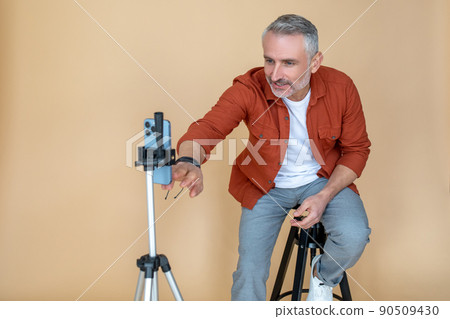 A man in a red jacket sitting on a stool in a studio and making selfie A man in a red jacket sitting on a stool in a studio and making selfie 90509430